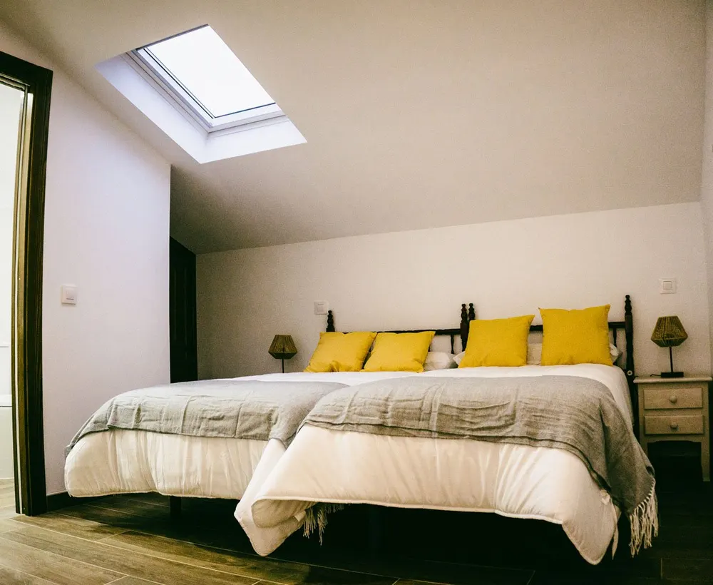 Dormitorio abuhardillado con claraboya y cojines amarillos