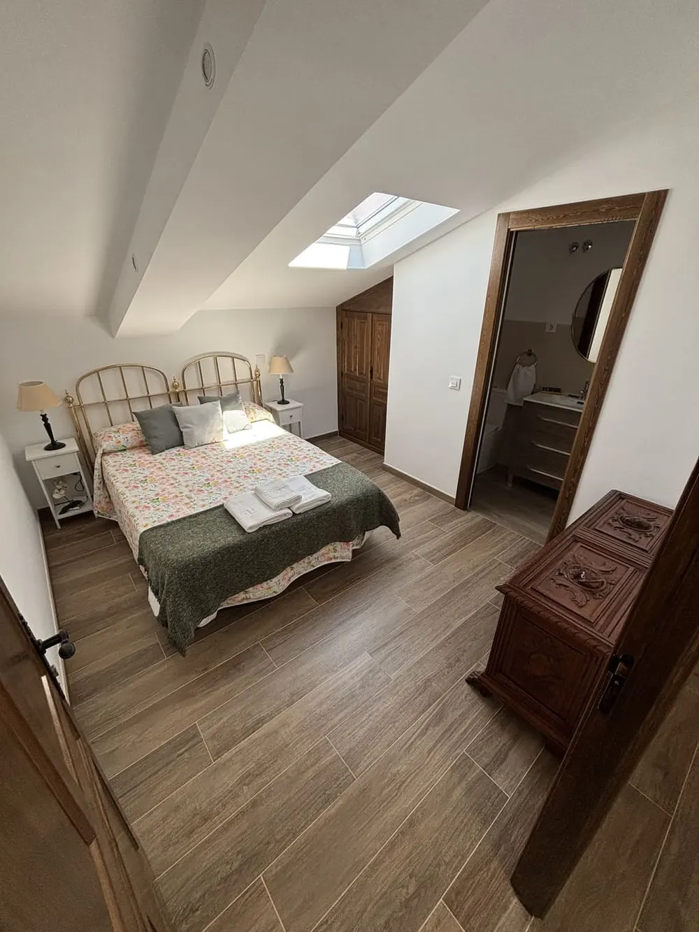 Dormitorio doble con cabecero de forja verde y toallas sobre la cama