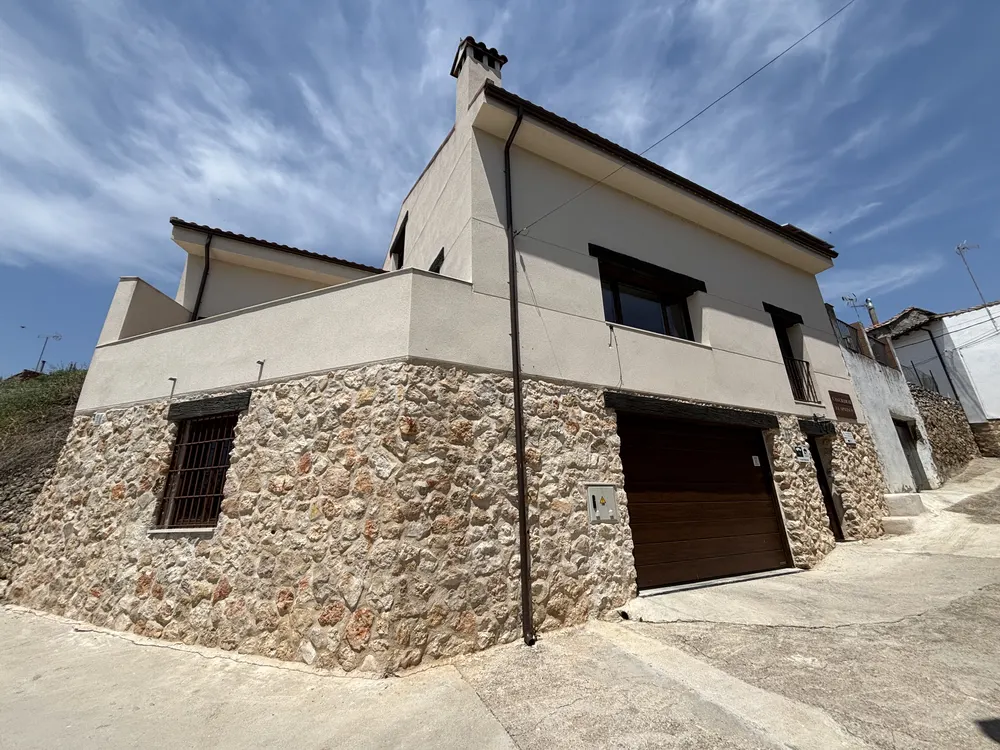 Fachada de piedra de Casa Rural El Aprisco con su cartel y el garaje