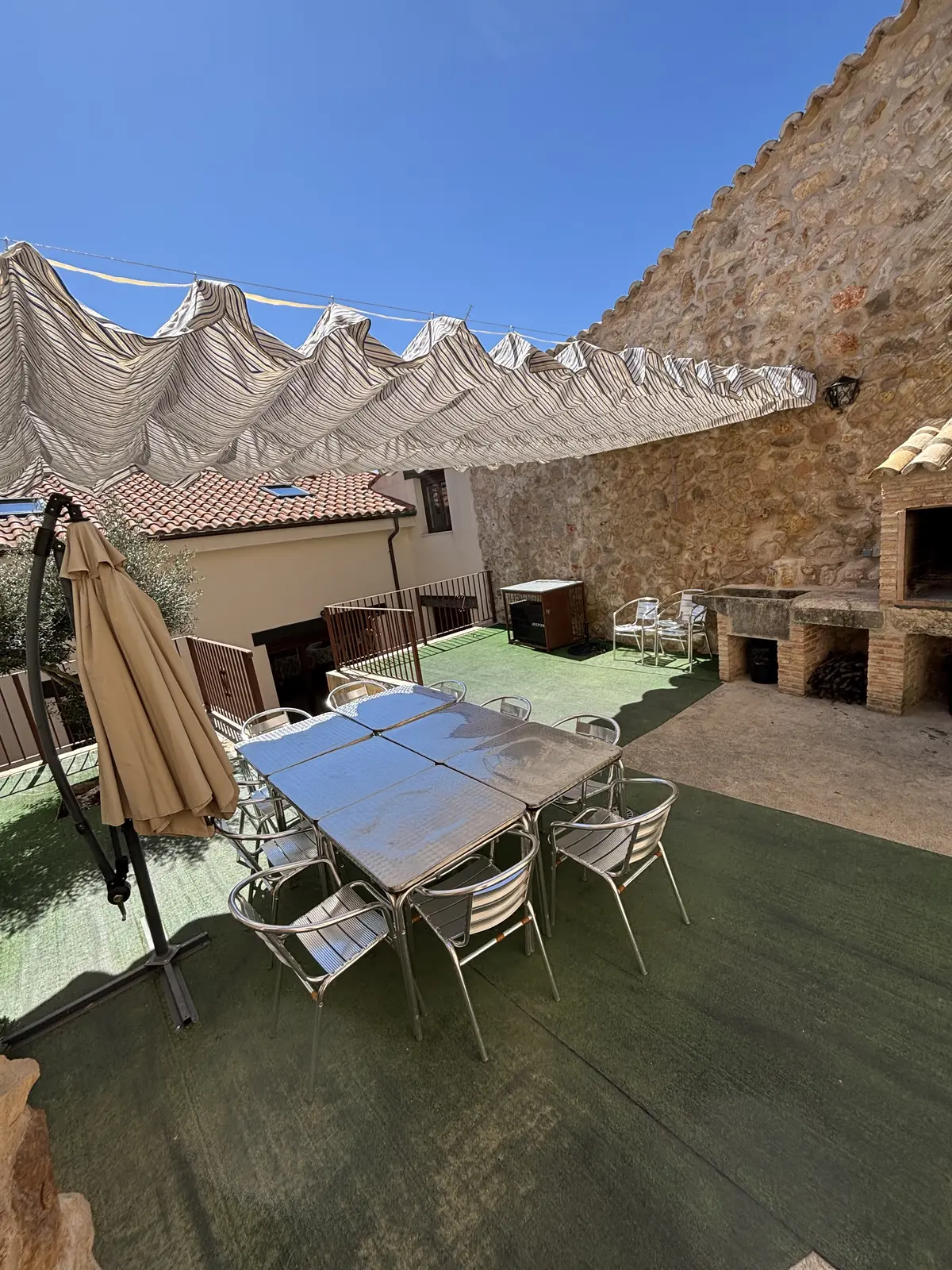 Mesa larga del patio preparada junto a la barbacoa de obra, bajo el toldo