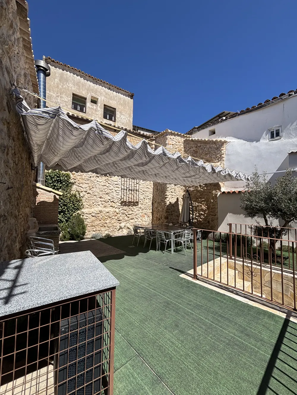 Cenador del patio con toldo y mesa junto al muro de piedra