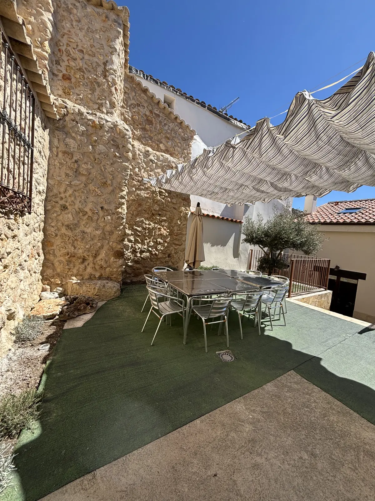 Mesa y sillas del patio bajo el toldo, junto al muro de piedra
