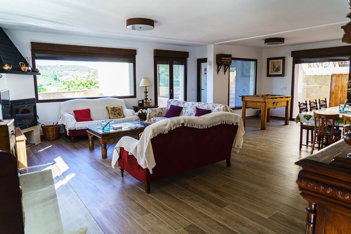 Salón comedor de El Aprisco con chimenea de leña y grandes ventanales con vistas al campo